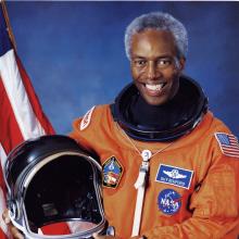 Guion Bluford, an African-American male astronaut, poses formally in an astronaut suit with his helmet.