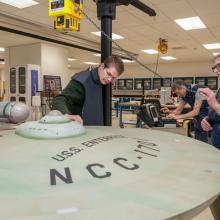 Three Smithsonian staff members use an X-ray machine to take images of the interior of a dish-shaped spaceship studio model.