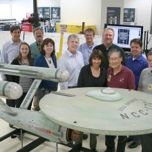 A group of Museum employees in charge of handling a gray spaceship studio model from the Star Trek series stand behind the studio model.