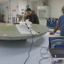 Two Museum specialists test lighting to match the original lighting as part of a gray spaceship studio model used in the Star Trek television series.