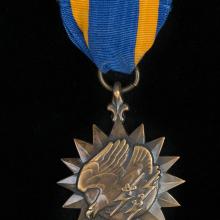 Bronze sunburst medal with eagle holding lightning bolts on blue silk ribbon with gold stripes