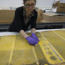 Conservator with purple gloves works over yellow rudder fabric.