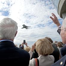 A group of people watch as the Space Shuttle Discovery, attached to a larger Boeing aircraft, flies low to the ground above the Steven F. Udvar-Hazy Center.