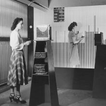 Two women stand at larger boards. 