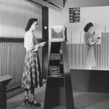 Two women stand at larger boards. 