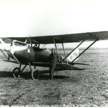 Black and white photograph of airplane with pilot in front.