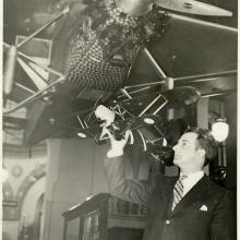 Man holding model of plane underneath hanging aircraft