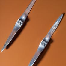 Two metal miniature propellers against an orange-red backdrop. 