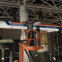 Staff on a lift work to lower a missile attached to the ceiling. 