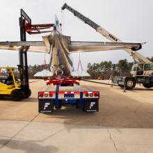 The Douglas DC-3 is being placed on a truck. People are on both sides guiding the process. 