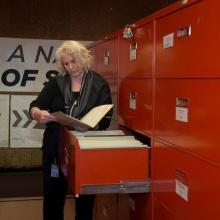 An archivist looks at a file while standing in front of a filing cabinet