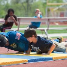 An astronaut and a student do push-ups outside. 