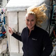 Kate Rubins in space next to sign that says ISS Voting Booth