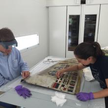 Two conservators work on a airplane cowling. 