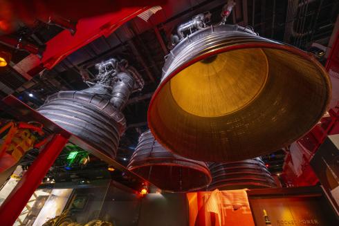 A huge engine hangs from the ceiling in front of a mirror, giving the effect of multiple engines. It is lit from below giving a warm glow of a rocket about to blast off. 