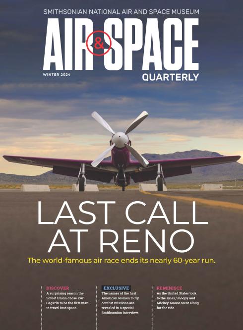 A small purple-painted airplane is parked on the pavement at Reno-Stead Airport, which is surrounded by mountains. The airplane's single engine is powered by a four-blade propeller.