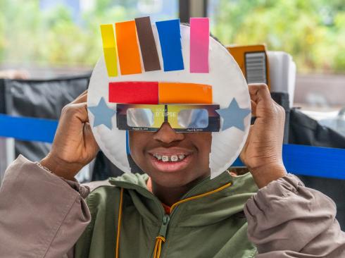 A young man shows off his eclipse viewing mask, created by adding a paper plate to eclipse glasses. 