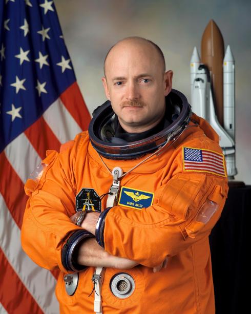 Mark Kelly poses in an orange pressurized astronaut suit for an official photo.