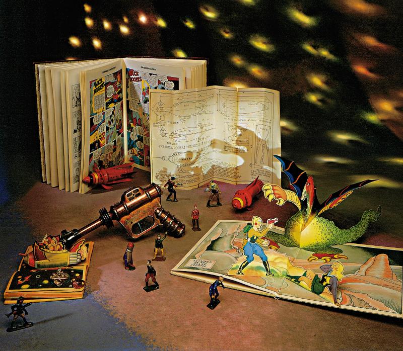 A collection of space-themed toys and comic books on a table with stars projected in the background.