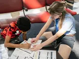 A participant in the summer camp works on calculations, sitting near the floor. 