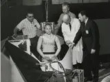 Man sits inside a centrifuge pod, four others surround him. 