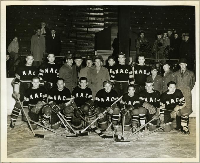 A group of men pose wearing hockey uniforms. Some of the men are holding hockey sticks.