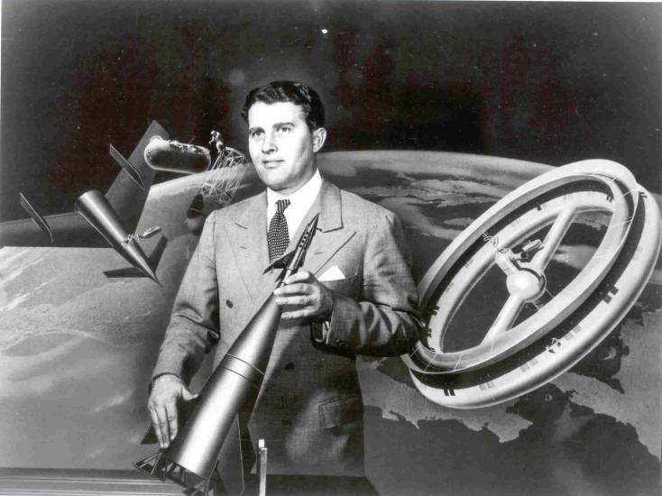 A man holds a model of a rocket in front of a painting of space.