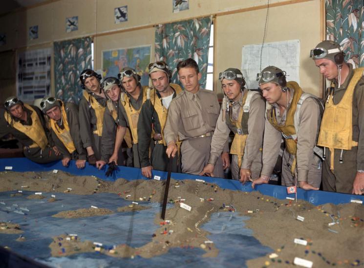 A line of men in uniform look at a 3D map.