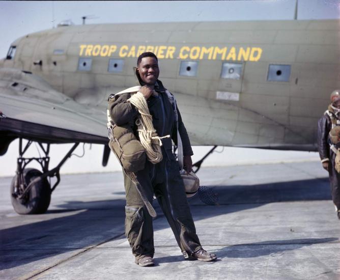 An African American man stands smiling in front of an olive drab airplane.