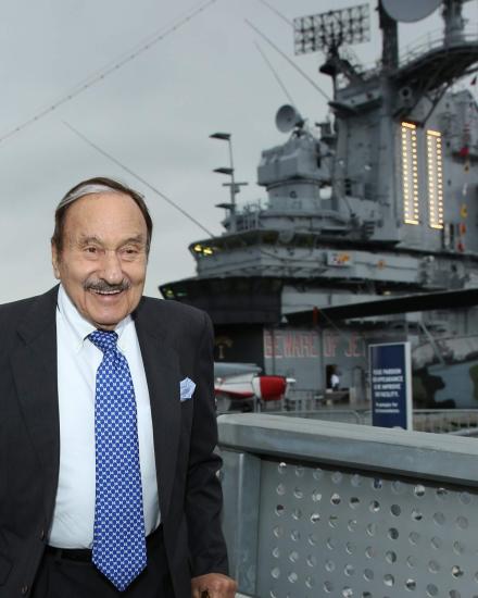 A man stands smiling in front of a ship. 