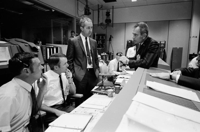 Four men stand around a console and talk