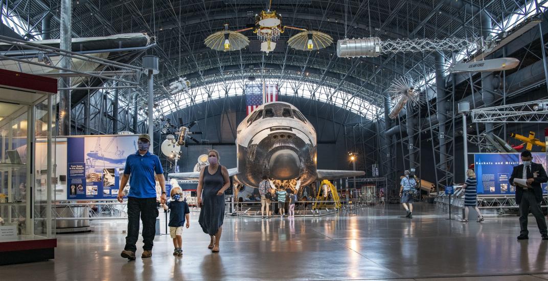 The Space Shuttle is visible in the background as masked visitors practice social distancing. 