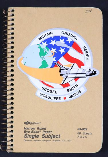 A spiral bound notebook with the Challenger mission patch on it. 