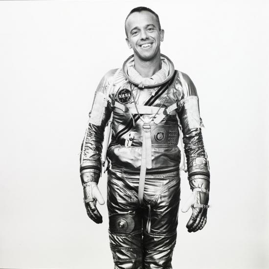 A man in a shiny spacesuit smiles at the camera.