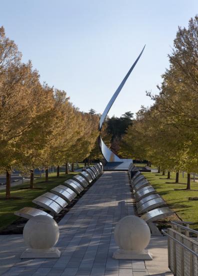 Tree lines path with a vertical swooping metal sculpture at the end