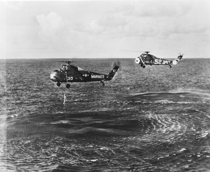 two helicopters fly over water