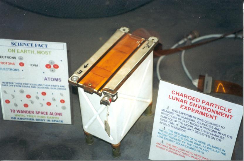 Photograph of the charged particle lunar environment experiment, which is shaped like a small rectangular box that is mostly white with orange on top. Two placards are next to the experiment to explain its function. 