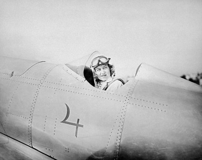 A woman in the cockpit of a plane looks behind her.