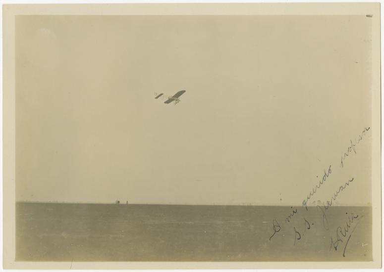 black and white photo One-half right rear view of monoplane in flight with the ground covering the bottom third of the image