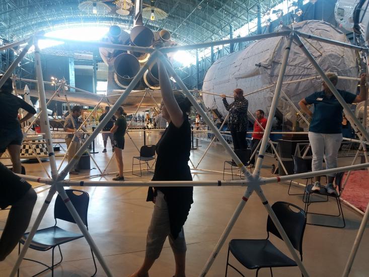 Teachers hold parts of a geodesic dome. A space shuttle is in the background.