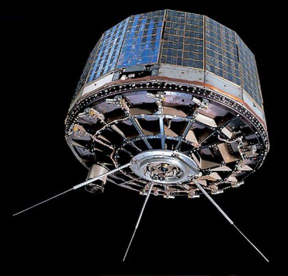 A column shaped satellite with metallic panels on the sides and three prongs emerging from the bottom.