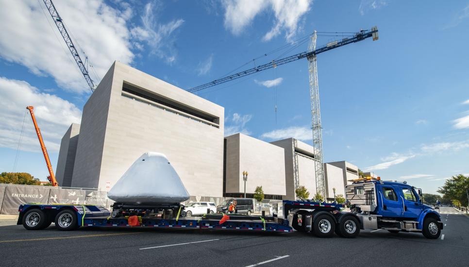 Command module Columbia at the back of a big truck with the National Air and Space Museum in the background.