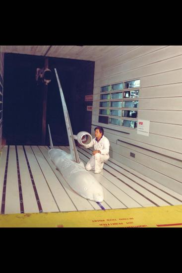 A photo of a man in a wind tunnel with a model of an airplane.