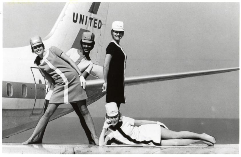 A black and white photograph of four female flight attendants posing in various positions in front of an aircraft.