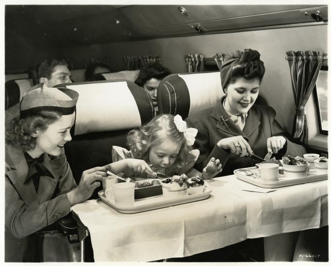 United Airlines flight attendant assisting passengers wearing the United Airlines flight attendant cap (1946)