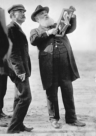 Alexander Graham Bell holding the handle of a kite and looking up into the air.