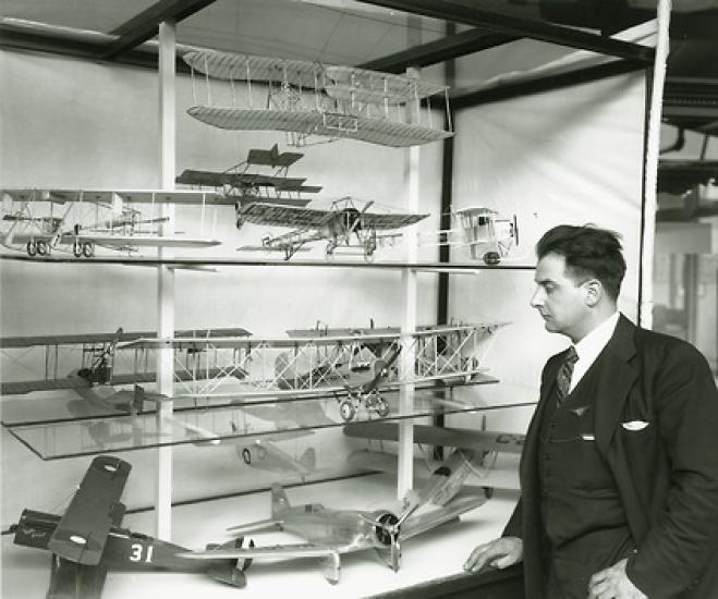 Paul Garber dressed in a suit looking at a cabinet containing airplane models.