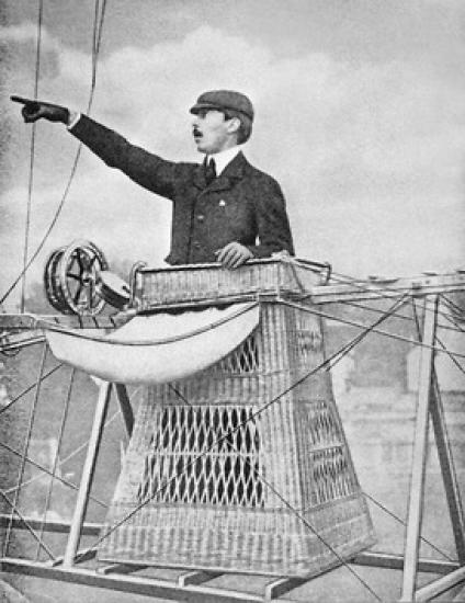 A man in basket-like airship gondola pointing to the left.