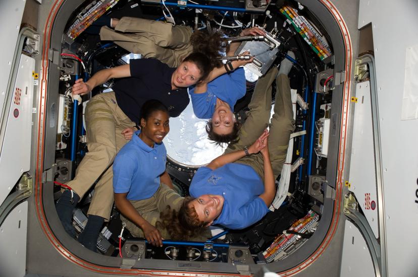 Four women in a space station forming a circular shape to fit in the small room.