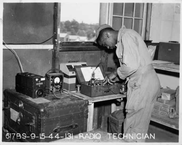 Black and white photograph of a man in uniform standing in front of radio equipment